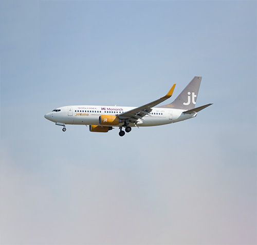 A white jet airliner with yellow accents in flight under a blue sky.