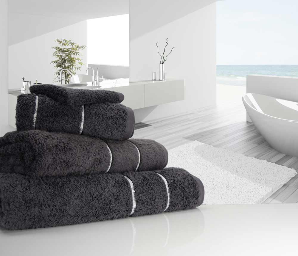 A pile of folded charcoal coloured 750 gsm Eqyptian Quality cotton towels place in a bathroom