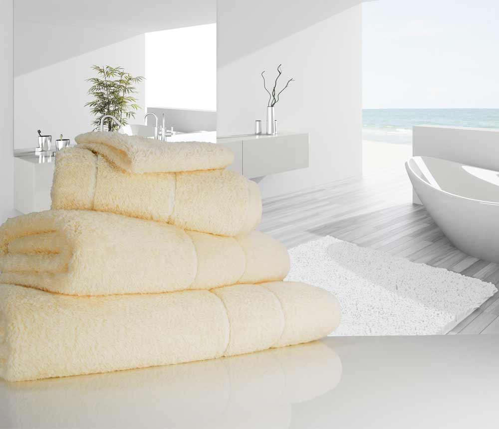 Neatly folded vanilla coloured 750 gsm Eqyptian Quality cotton towels near a bathtub
