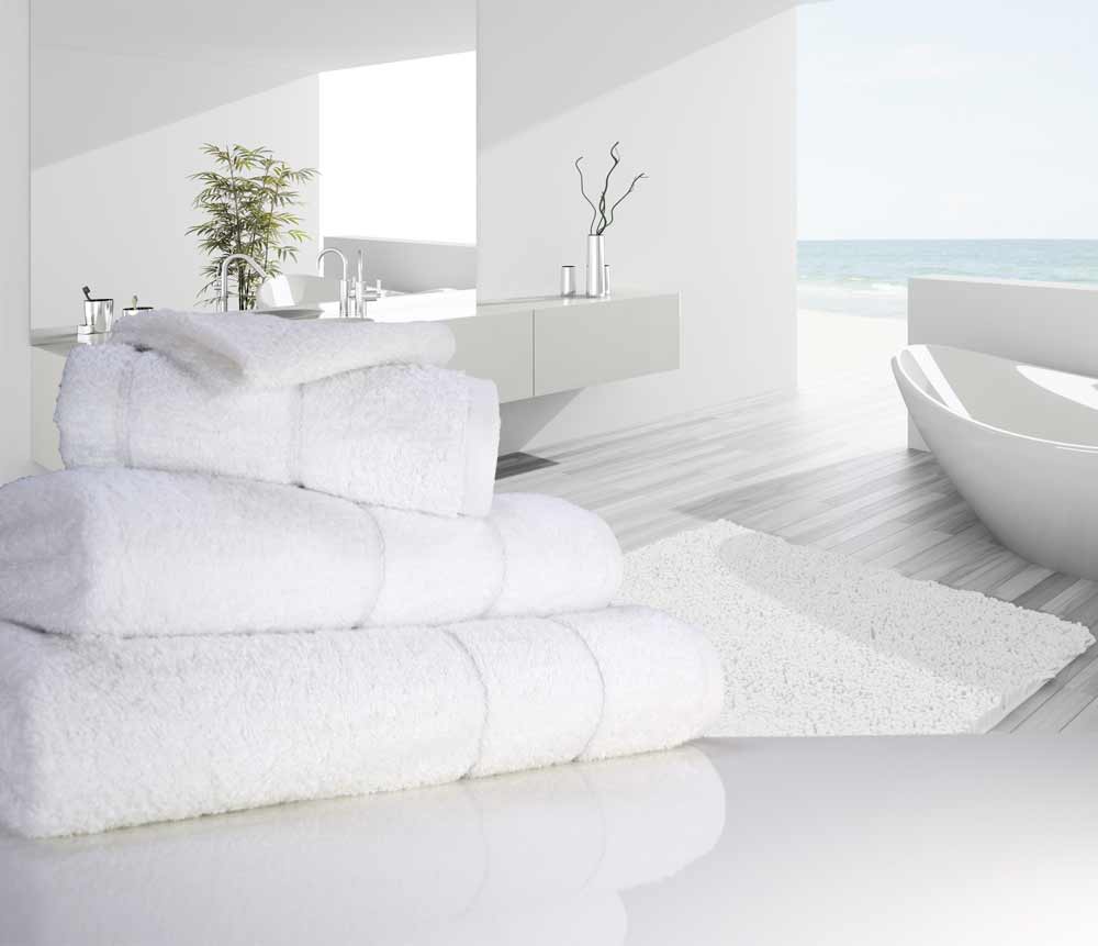Nicely folded white coloured 750 gsm Eqyptian cotton towels next to a bathtub