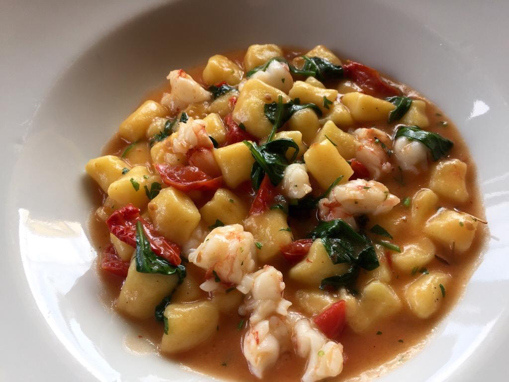 Gnocchi di patate con gamberi, spinaci e pomodori in salsa di pomodoro, serviti in una ciotola bianca.