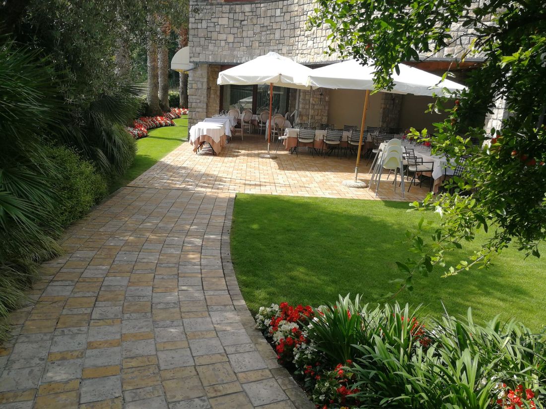 Sentiero in pietra che conduce alla zona pranzo all'aperto con ombrelloni e tavoli bianchi.