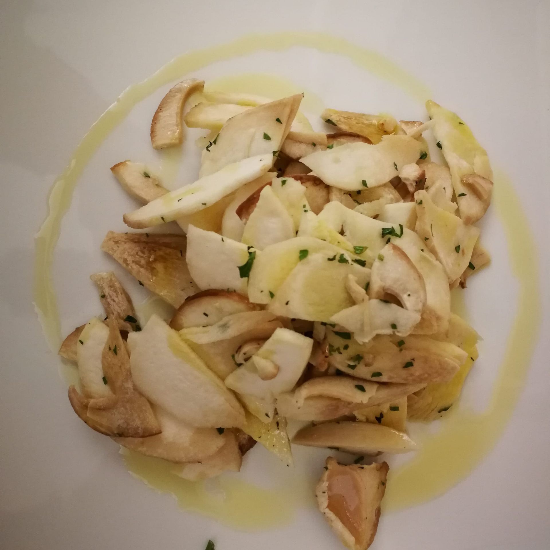 Funghi affettati, conditi con olio d'oliva e prezzemolo, su un piatto bianco.