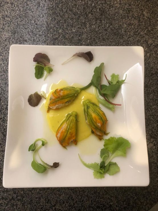 Piatto bianco quadrato con fiori di zucca fritti e salsa gialla, guarnito con verdure.