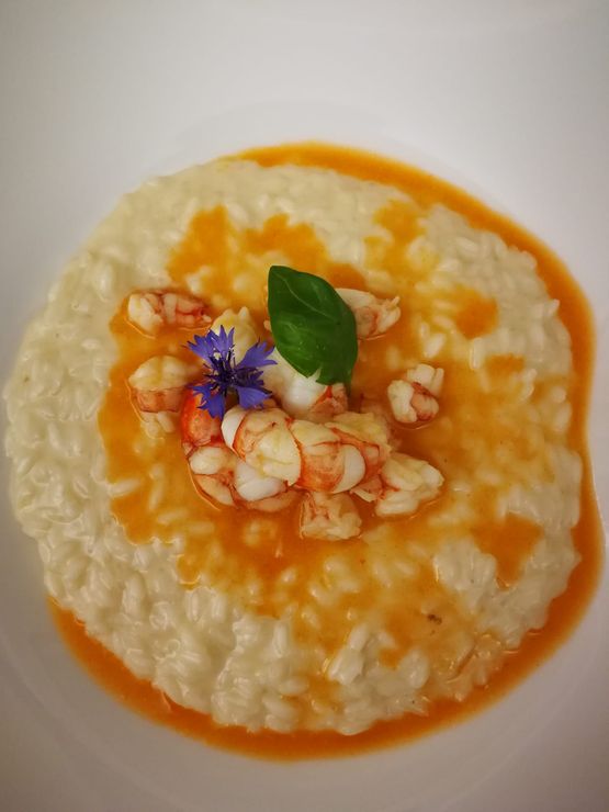 Risotto ai gamberi, condito con salsa all'arancia e guarnito con basilico e fiori.