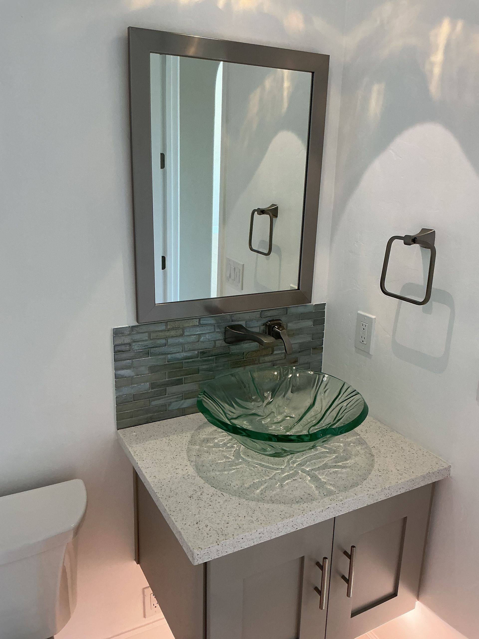 Bathroom with glass sink, gray countertop, mosaic backsplash, framed mirror, and chrome fixtures.