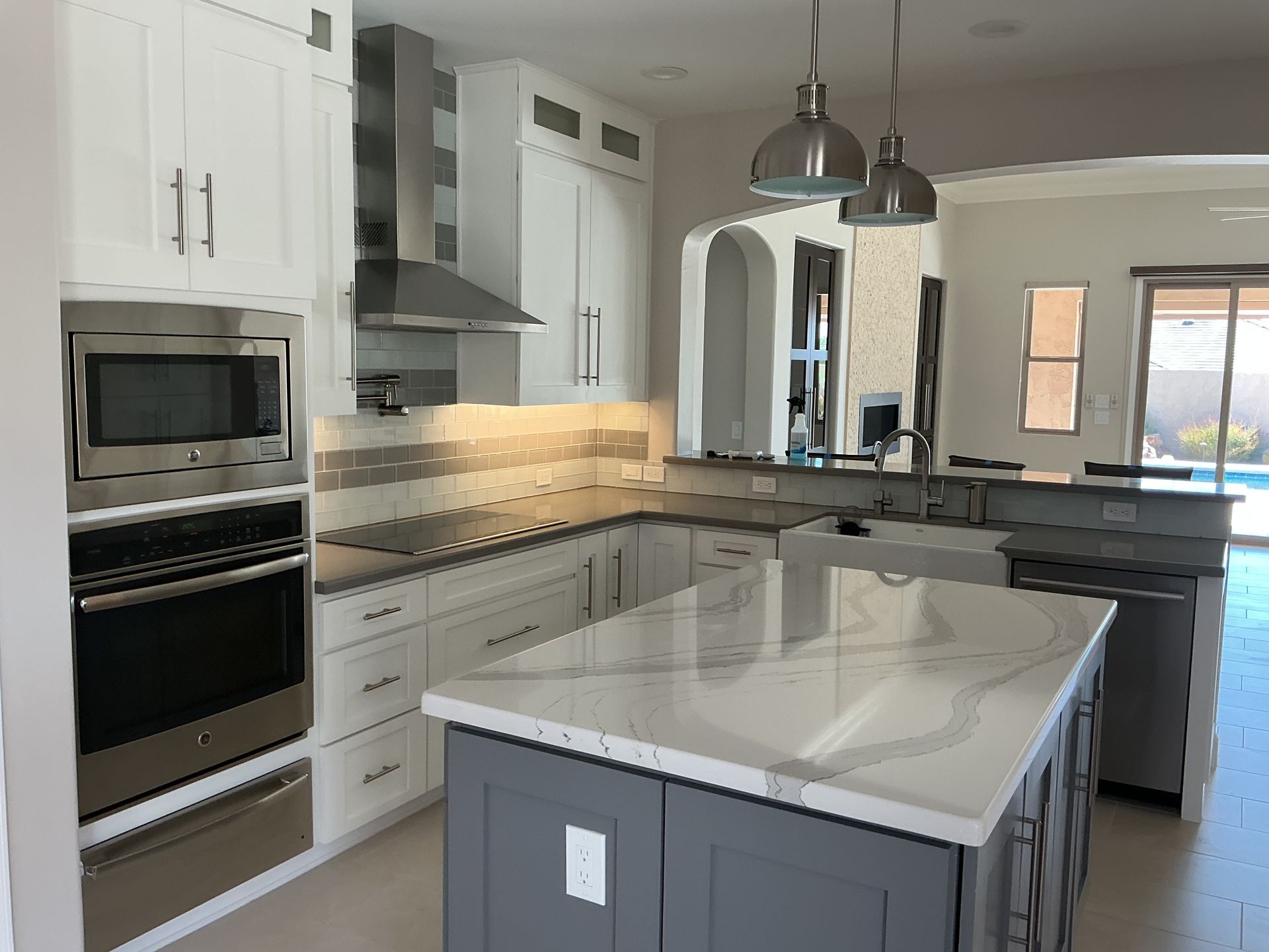Modern white kitchen with gray island, stainless steel appliances, and hanging lights.