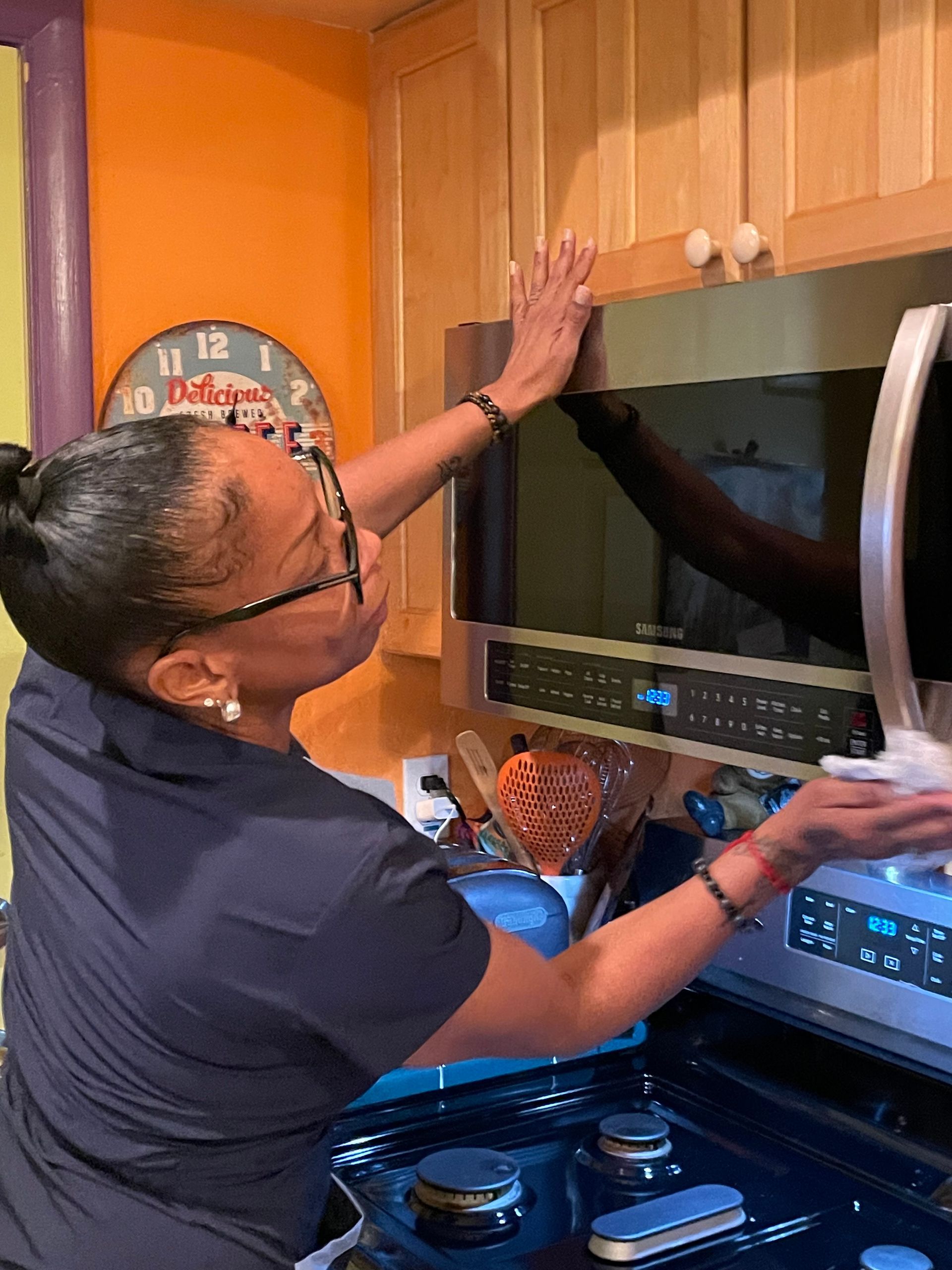 Woman cleaning microwave above stove in kitchen.