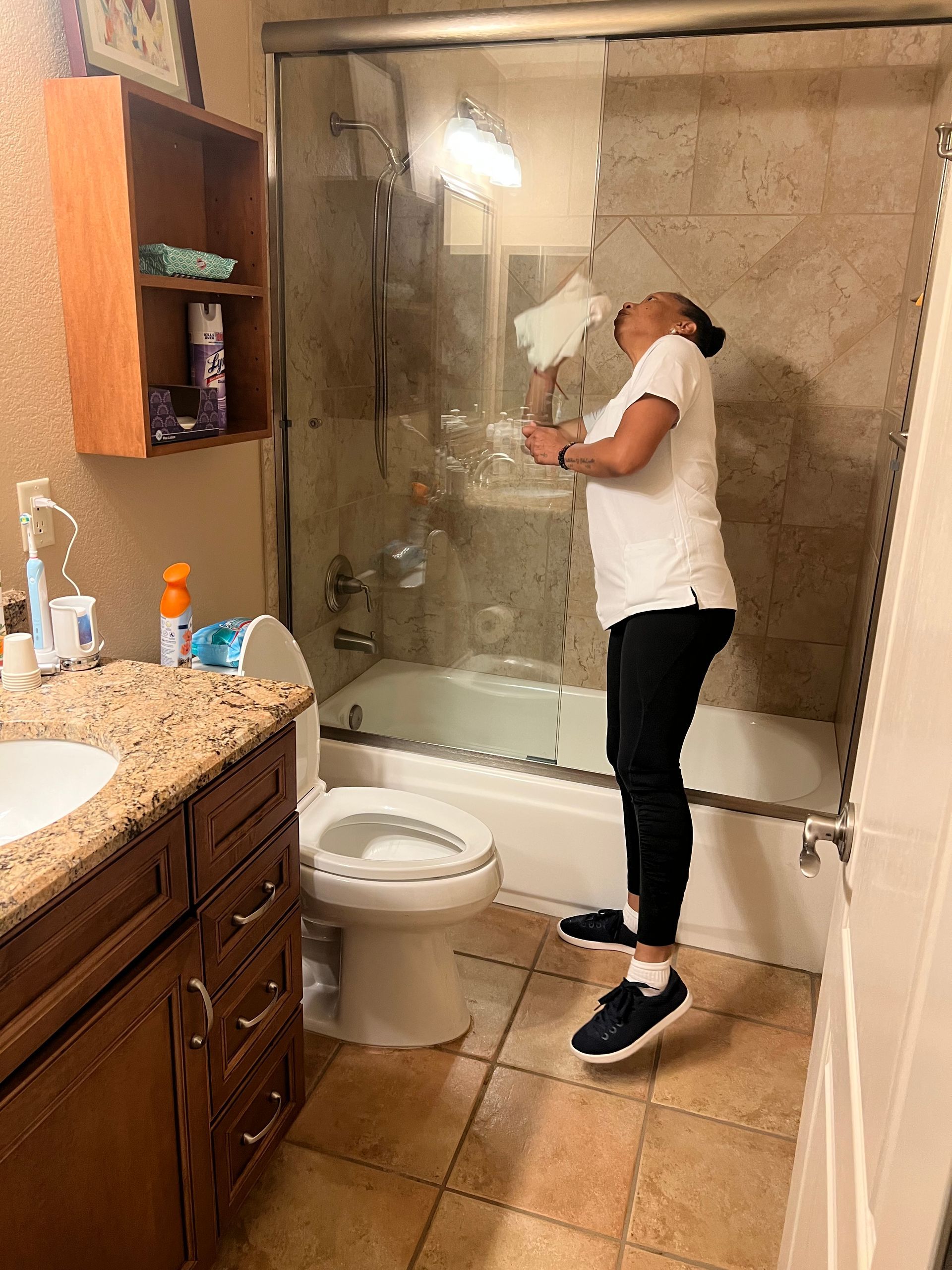 Person cleaning a shower in a bathroom. The person is reaching up with cleaning tools.