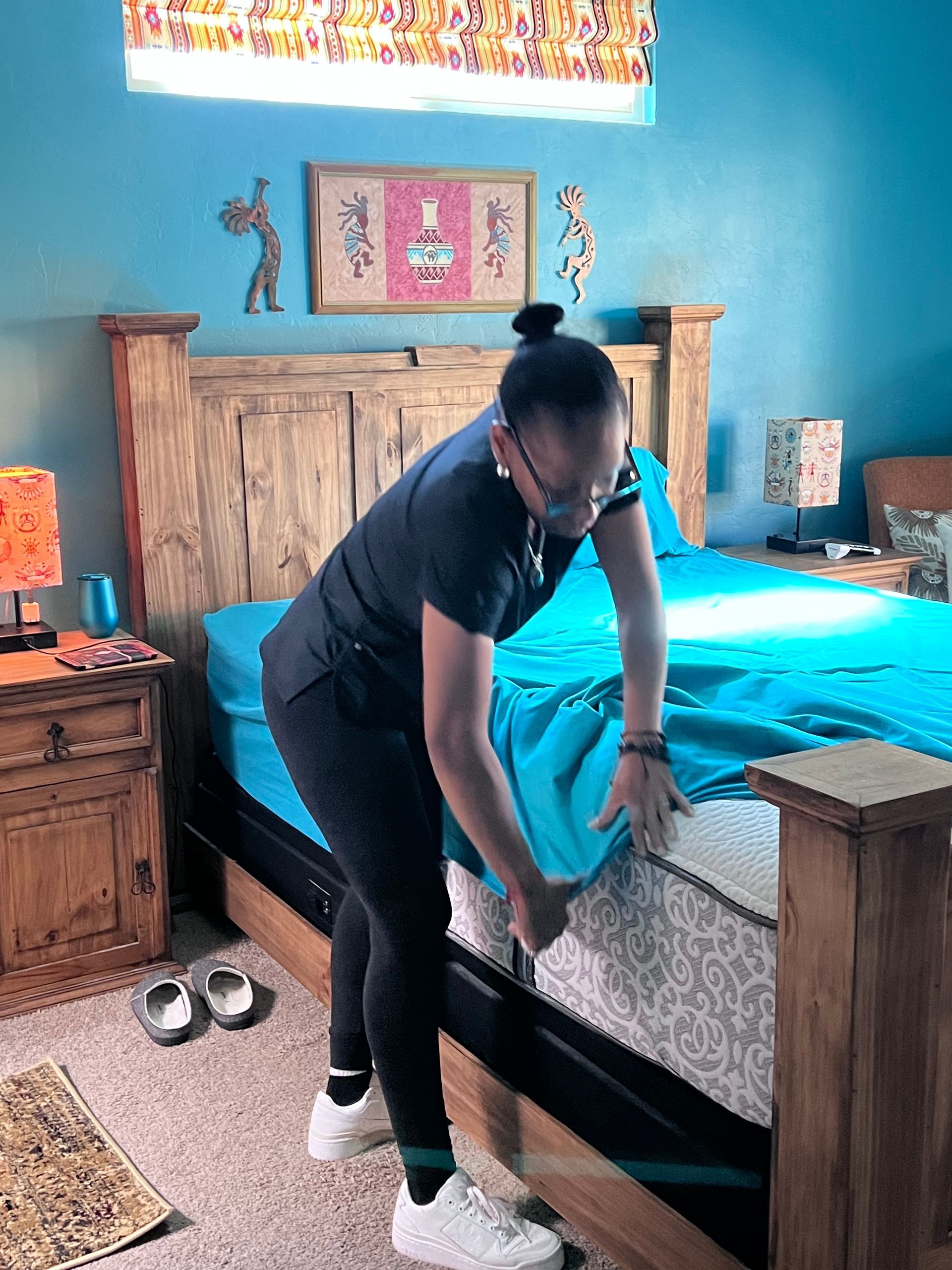 Person making a bed in a blue-walled bedroom, placing a turquoise sheet on the mattress.