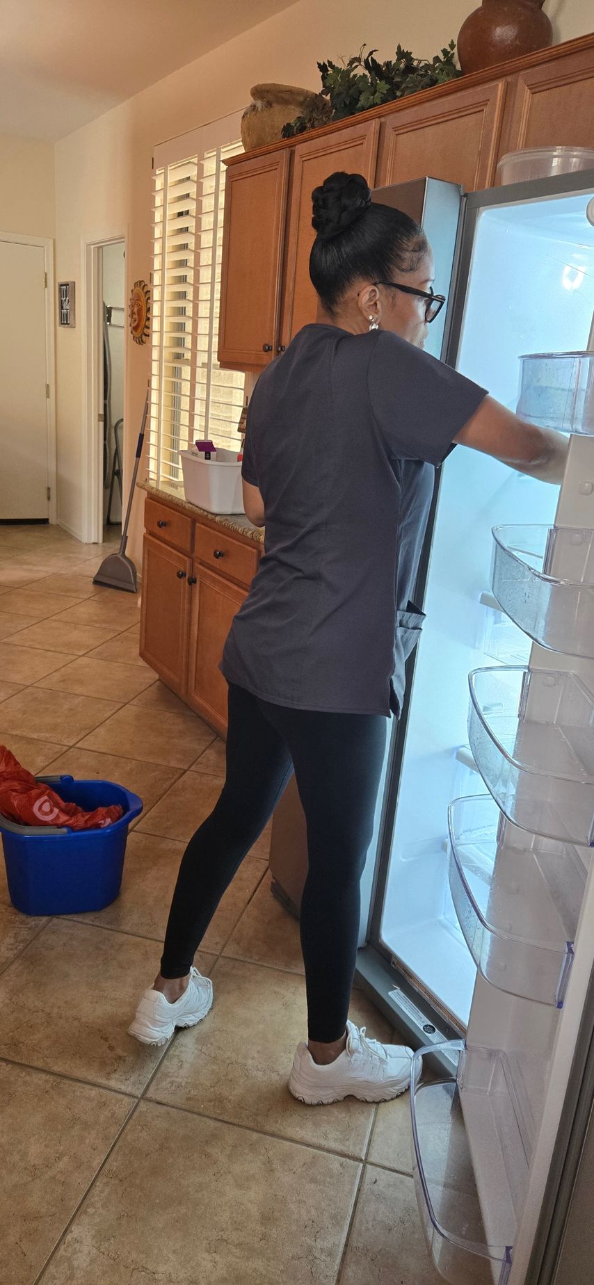 A person in a gray shirt and black pants opens a refrigerator in a kitchen.