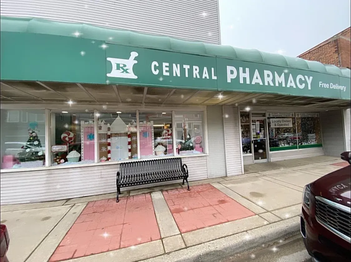 A pharmacy with a green awning and a bench in front of it.