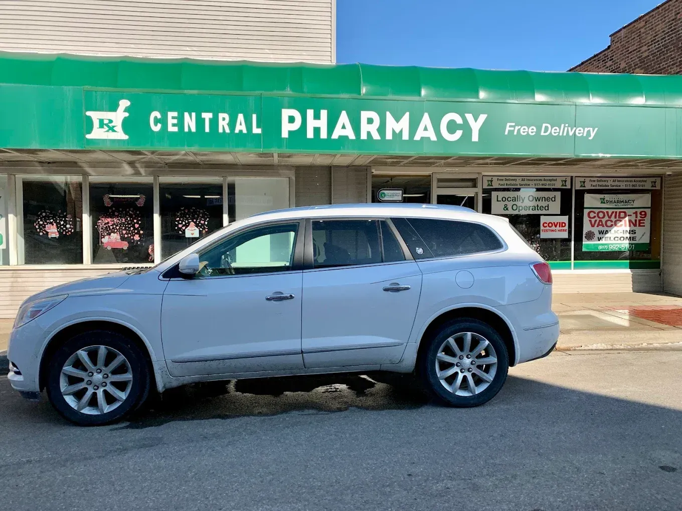 A white suv is parked in front of a pharmacy.