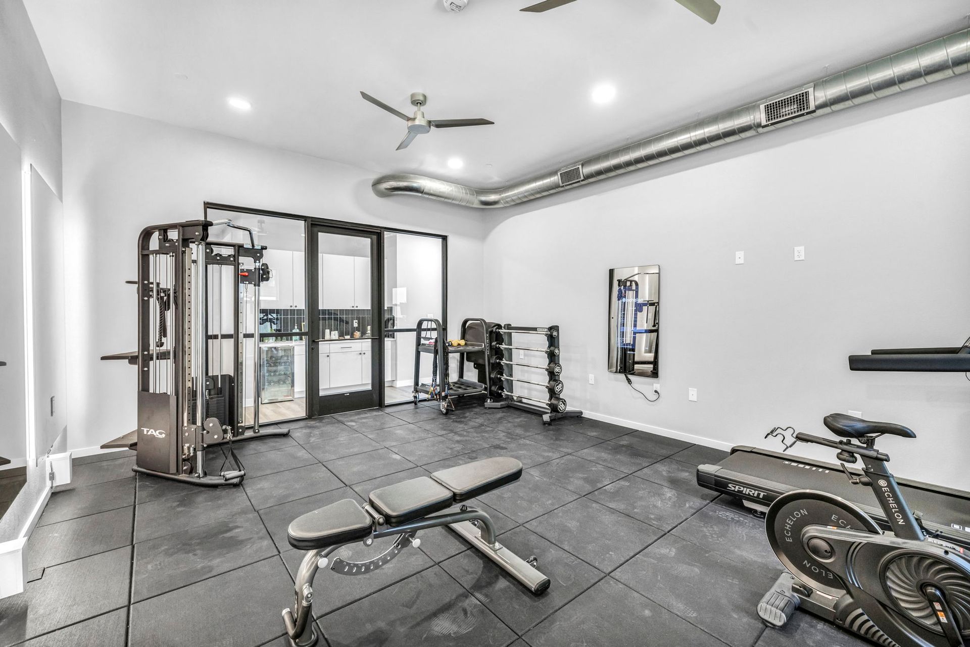 Modern home gym with weight bench, cable machine, mirrored wall, and stationary bike