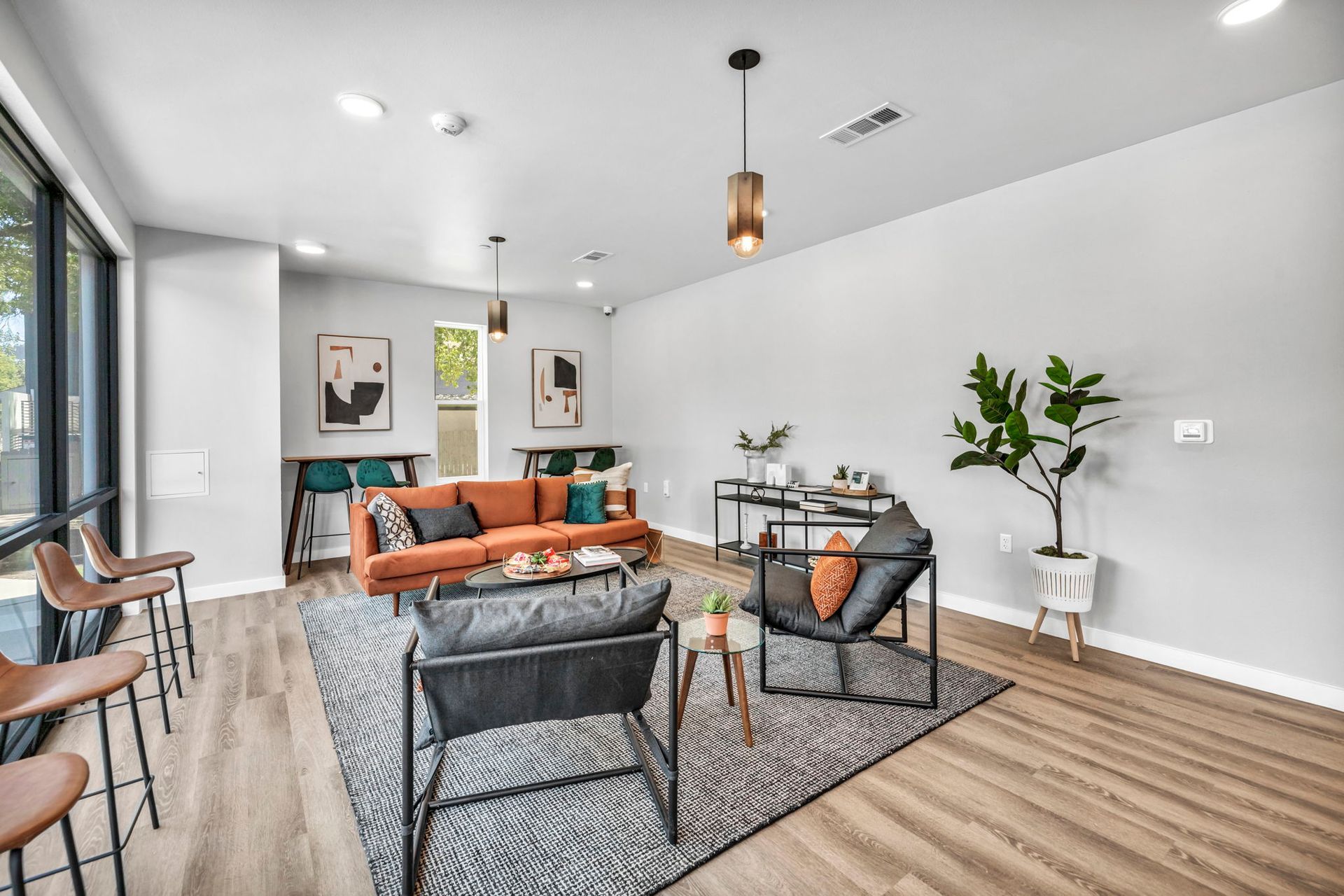Modern living room with orange sofa, black chairs, rug, wood floors, and large windows
