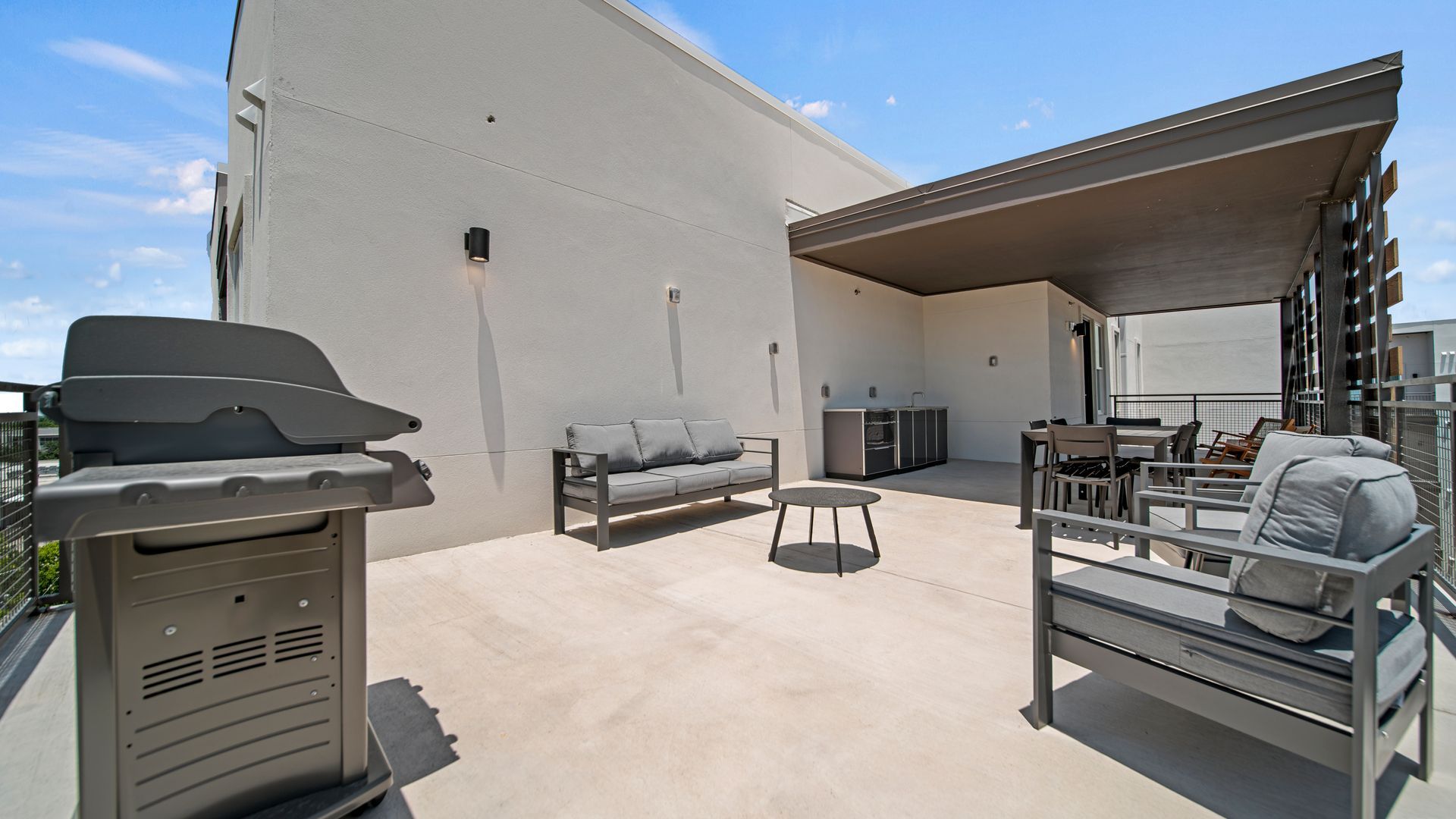 Rooftop patio with lounge chairs, grill, and shaded dining area under a blue sky