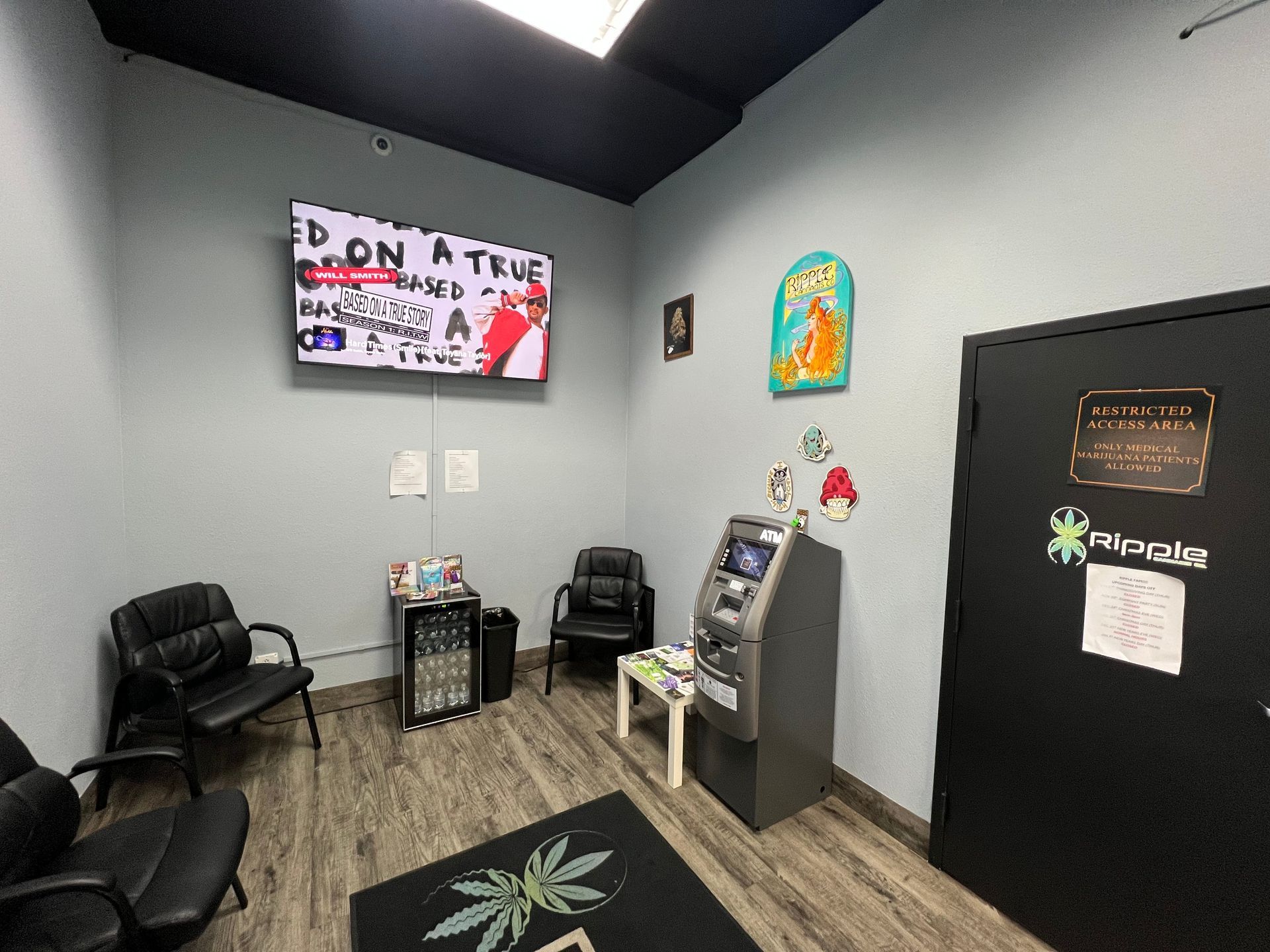 Waiting room with black chairs, TV, ATM, and black door, possibly a dispensary.