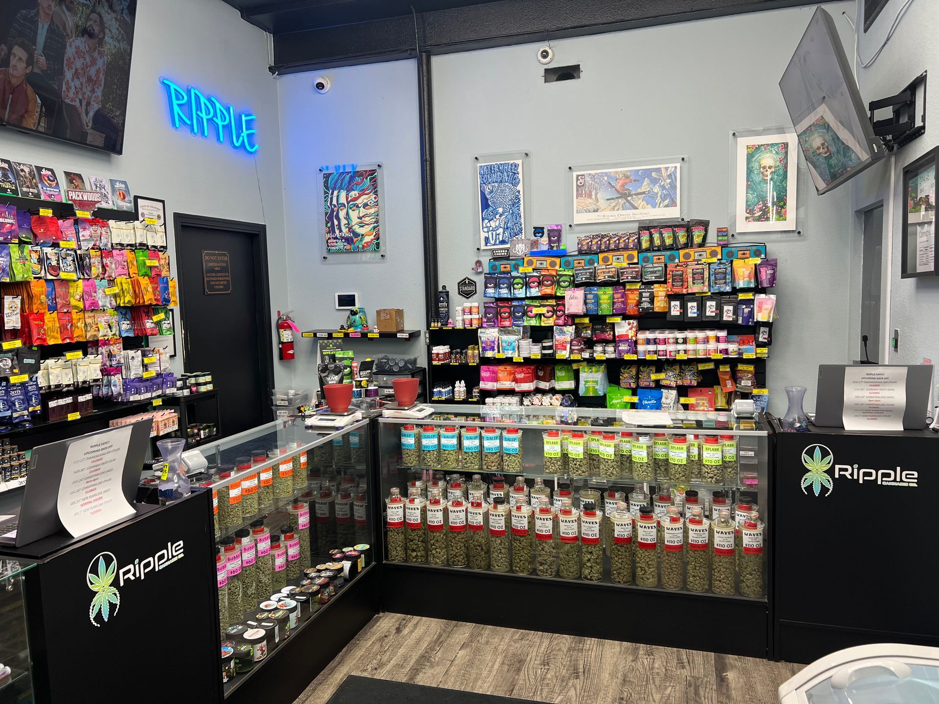 Interior of a cannabis dispensary with products behind glass counters and neon sign.