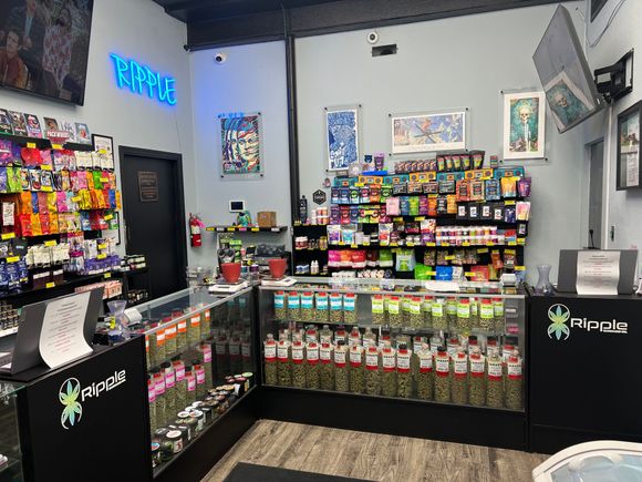 Interior of a cannabis dispensary with products behind glass counters and neon sign.