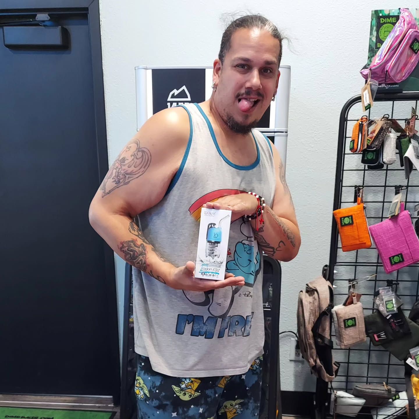 Man in a tank top holding a product, sticking his tongue out in a store.
