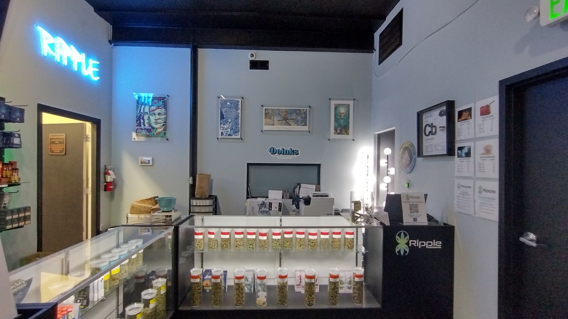 Interior of a cannabis dispensary with display cases, counter, and neon sign that reads 