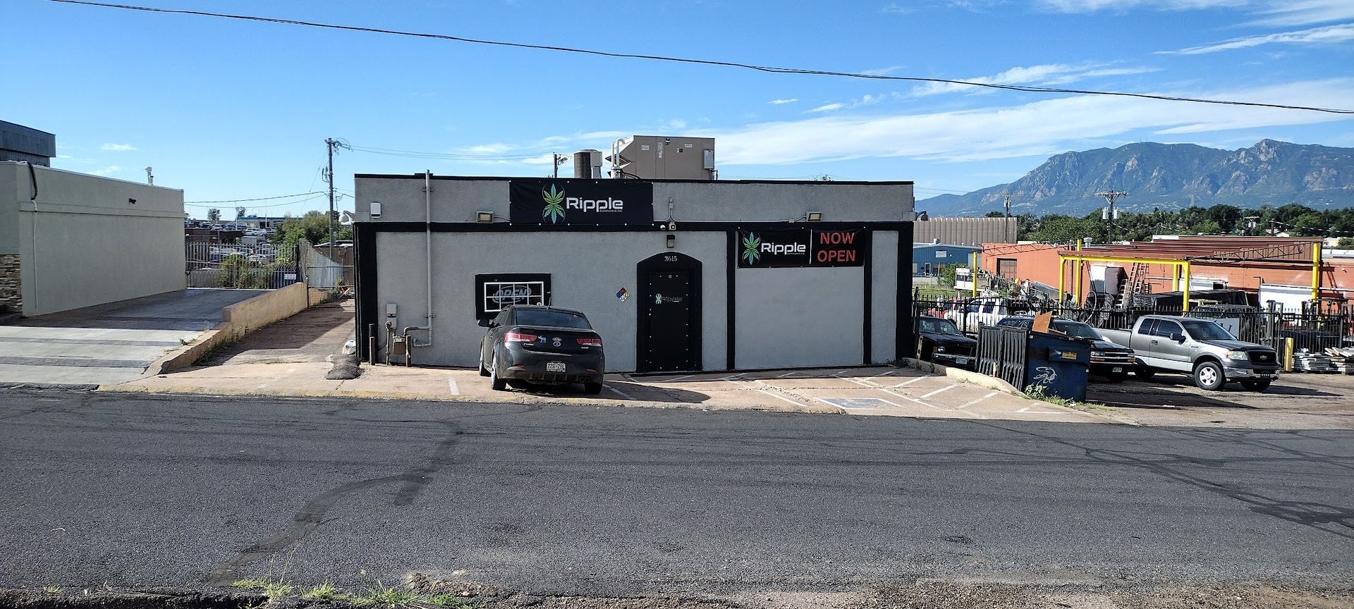 A single-story building with black trim and a black car parked in front. Mountains are in the background.