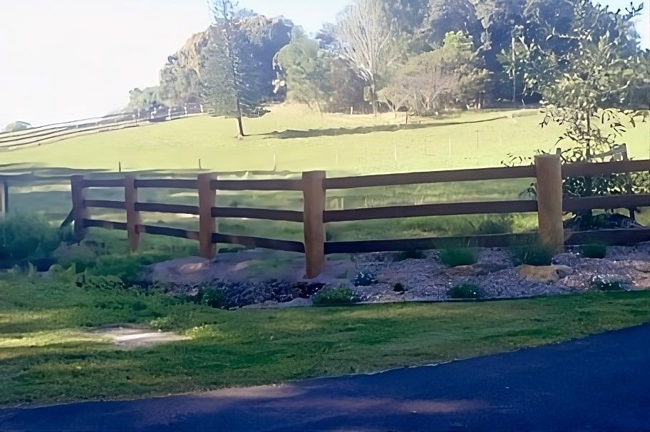 A Wooden Fence Surrounds A Grassy Field With Trees In The Background — John Stark Fencing In West Woombye, QLD