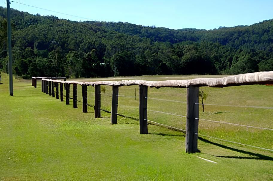 A Long Wooden Fence Surrounds A Grassy Field With Mountains In The Background — John Stark Fencing In West Woombye, QLD