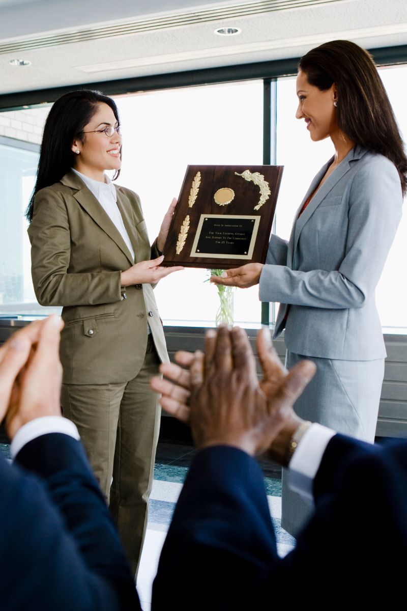 A woman in a suit is giving a plaque to another woman.