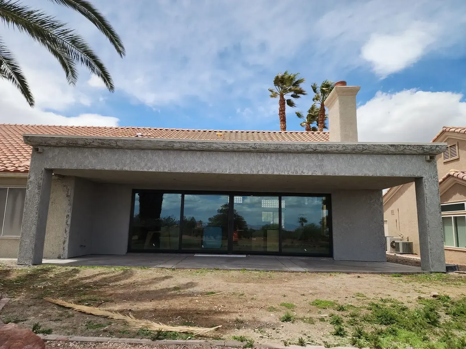 Rear view of a house with an attached patio, large sliding glass doors, and a chimney.