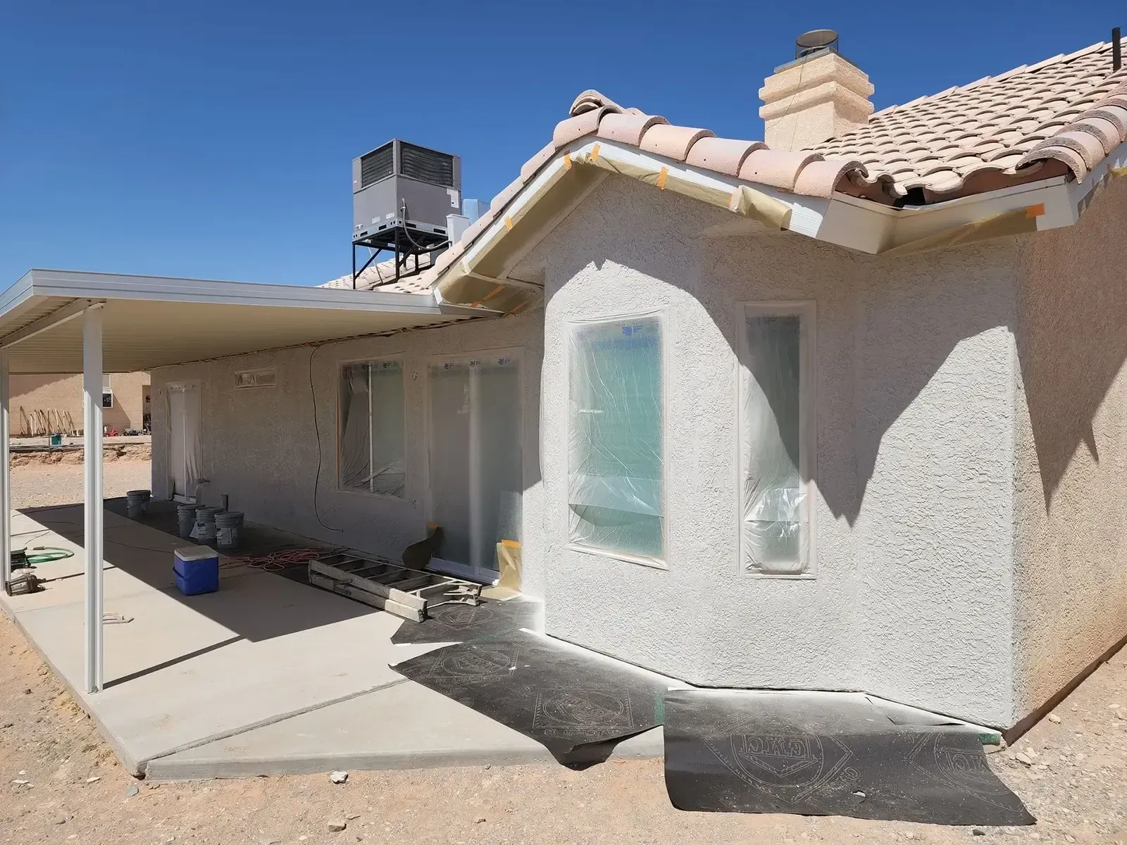 House exterior with stucco walls, windows covered, patio, and tan roof tiles on a sunny day.