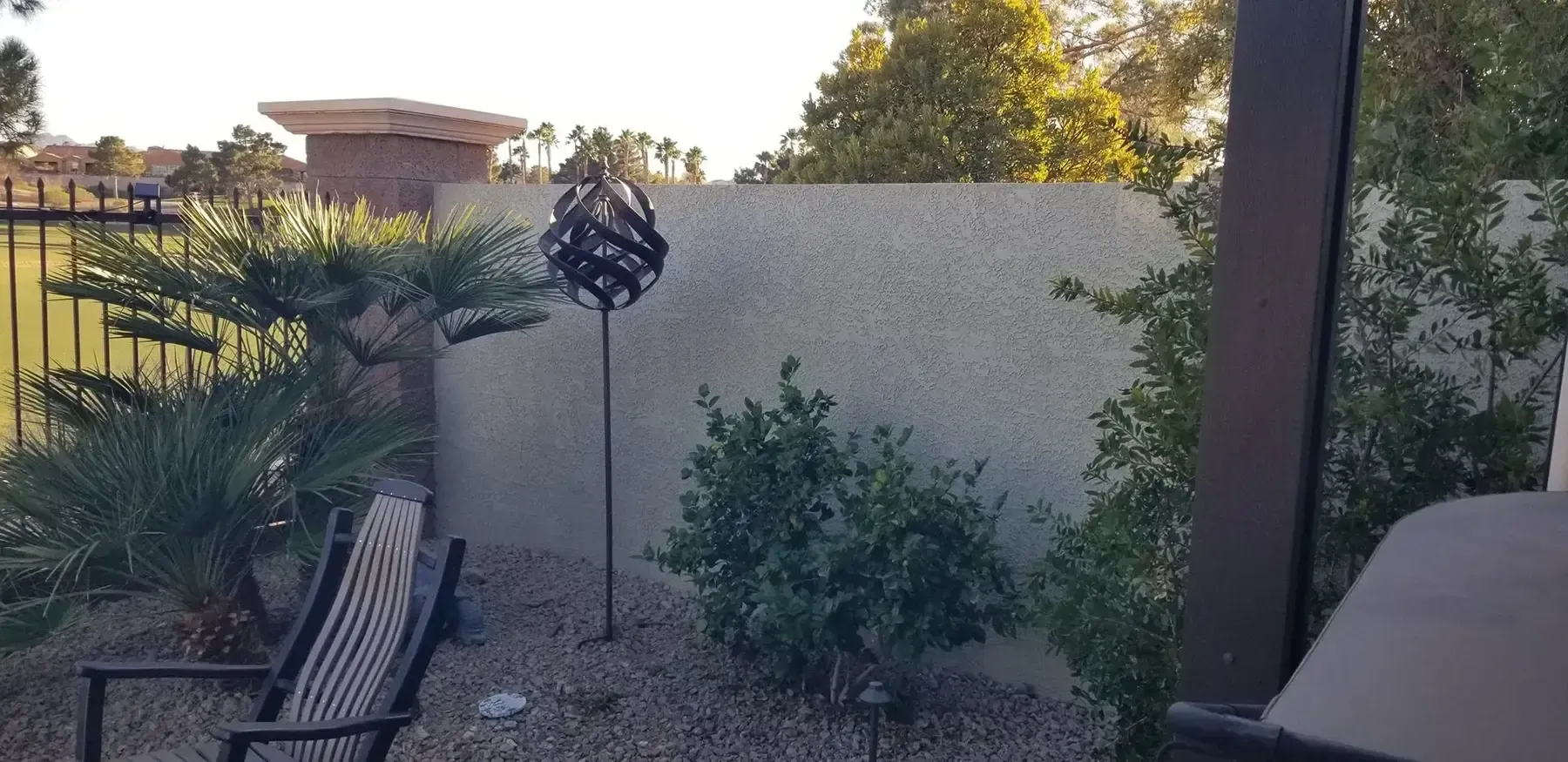 Backyard with a metal art sphere on a pole, trees, a wall, and a chair.