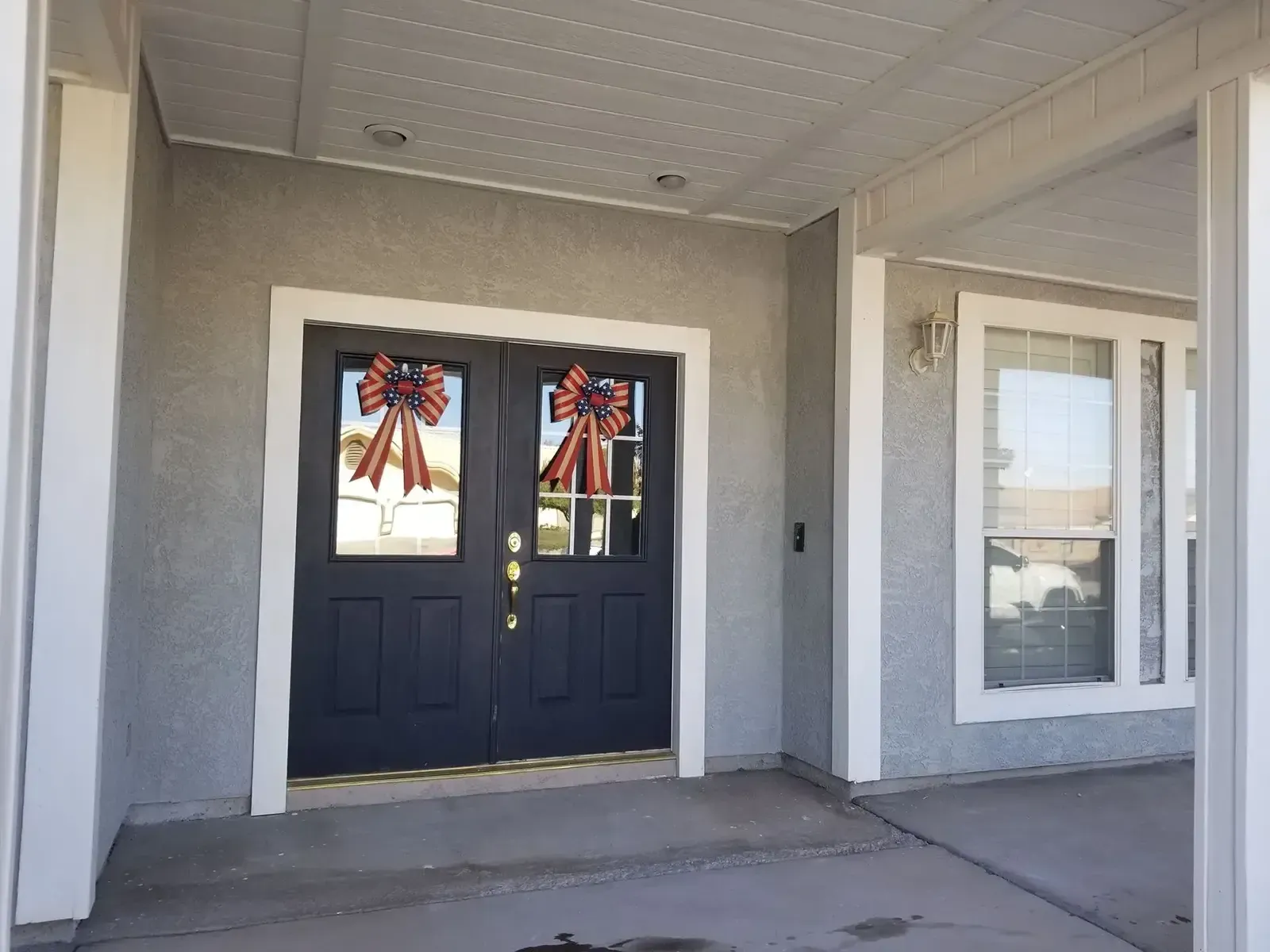 Exterior view of a home's entryway with dark double doors, white trim, and decorative bows.