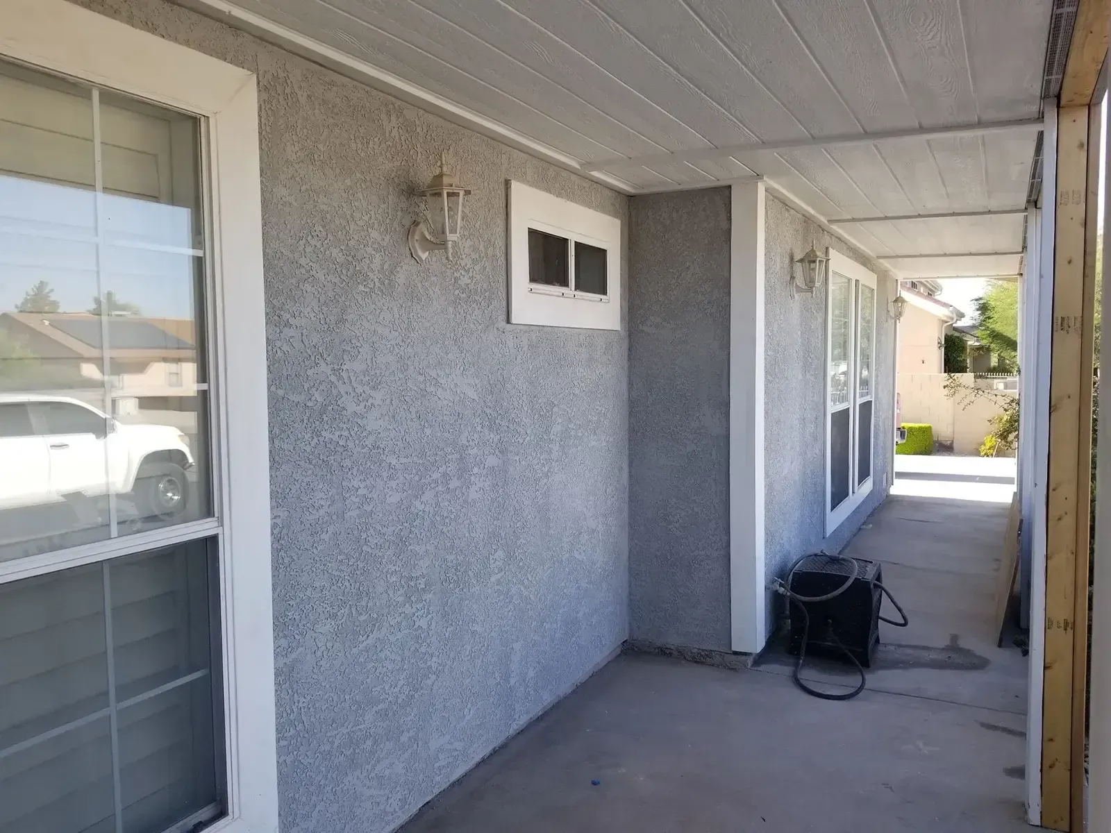 Covered porch with gray stucco walls, white trim, windows, and a ceiling.