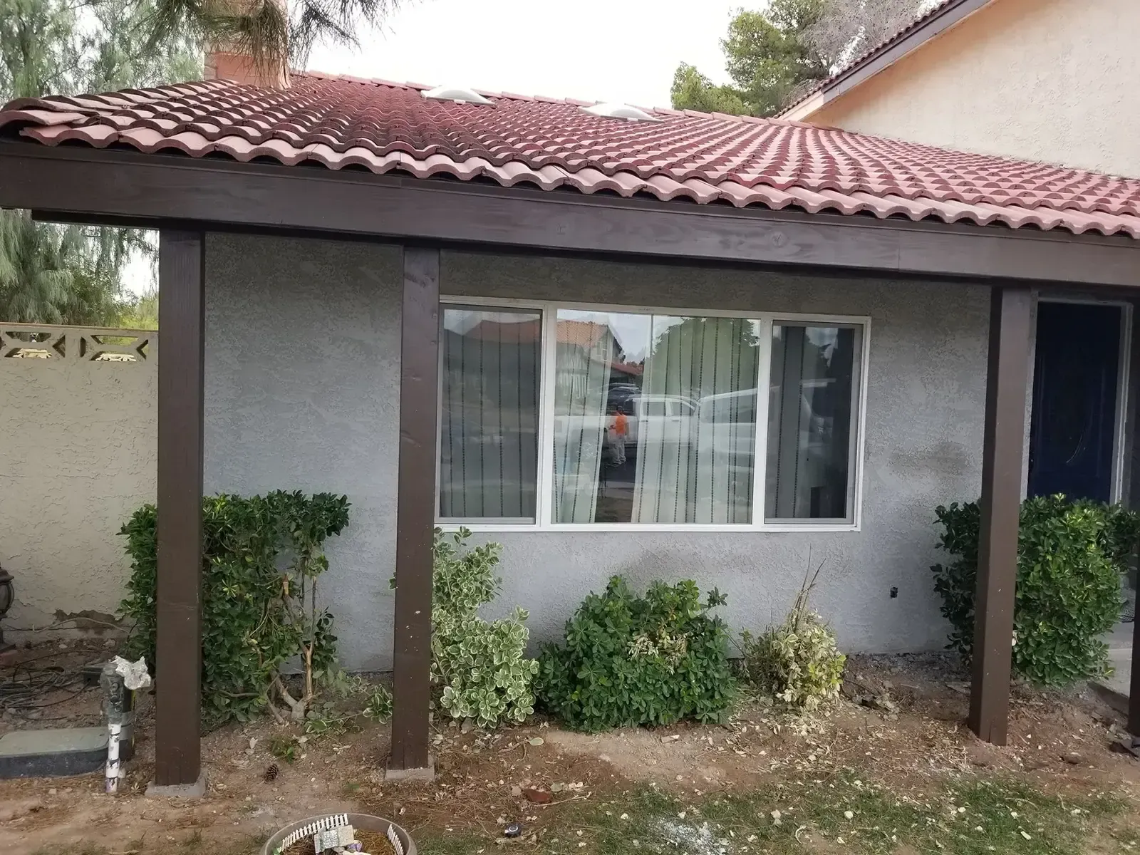 A brown-framed awning with a red-tiled roof shelters a window in a gray stucco building. 
