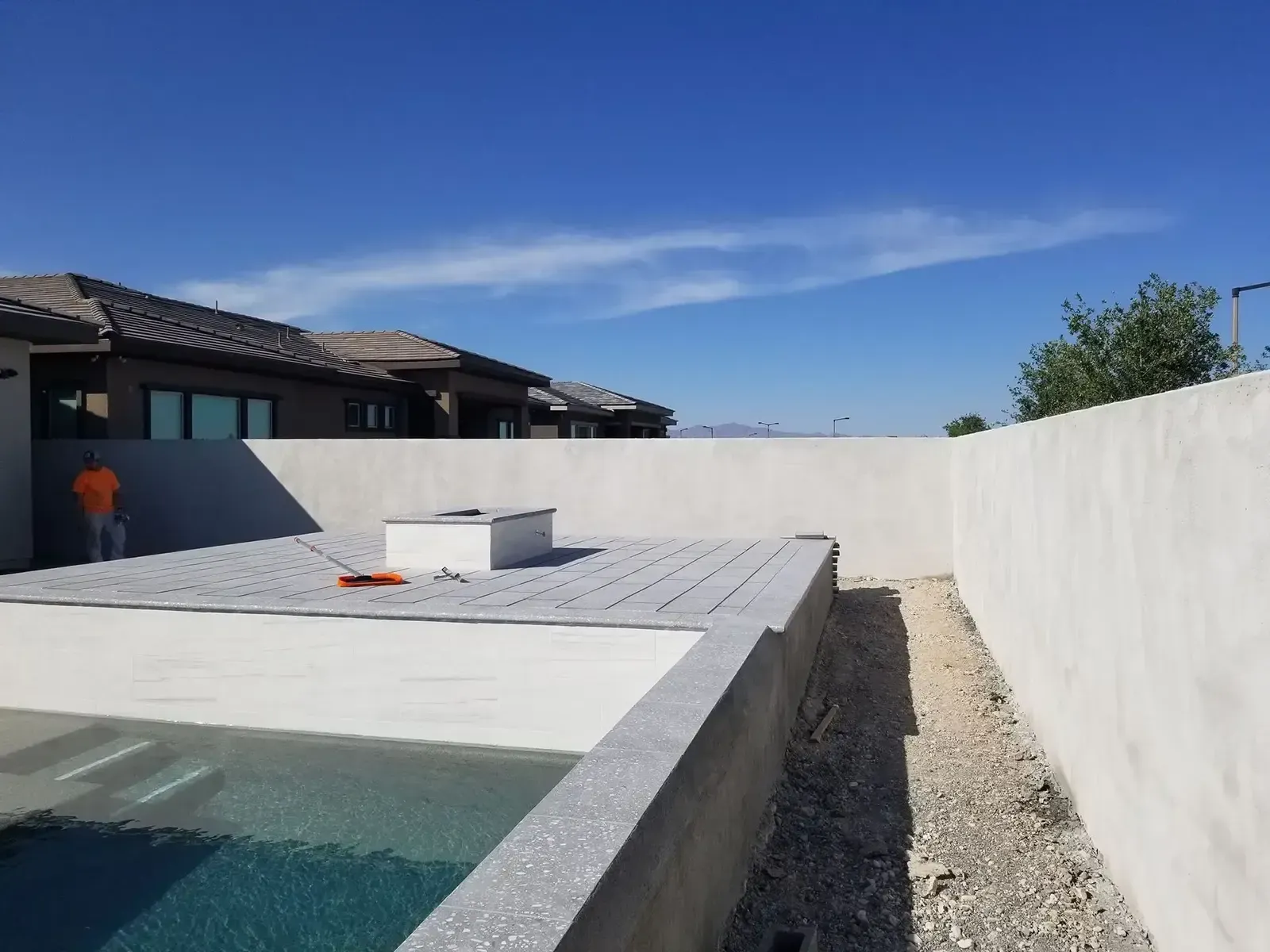 Pool area with a house in the background and a worker on the left.