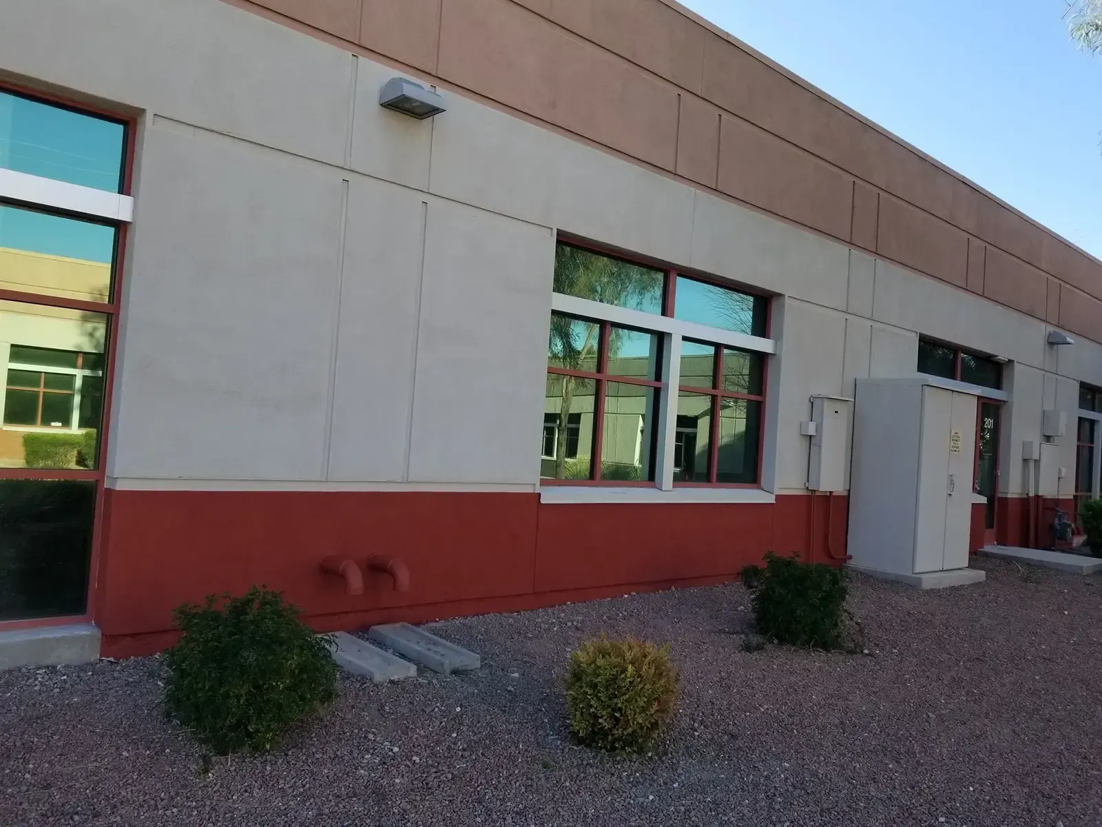 Tan and red building with reflective windows, small bushes, and gravel.
