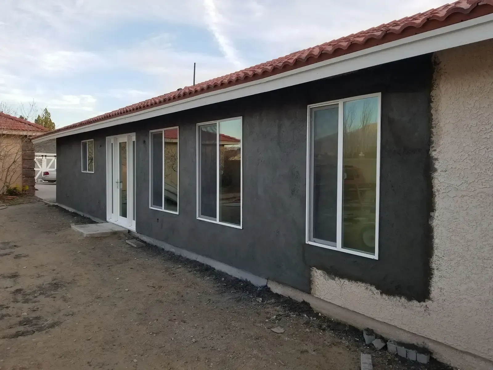 Exterior of a house with dark gray stucco siding and several windows under a terracotta tiled roof.