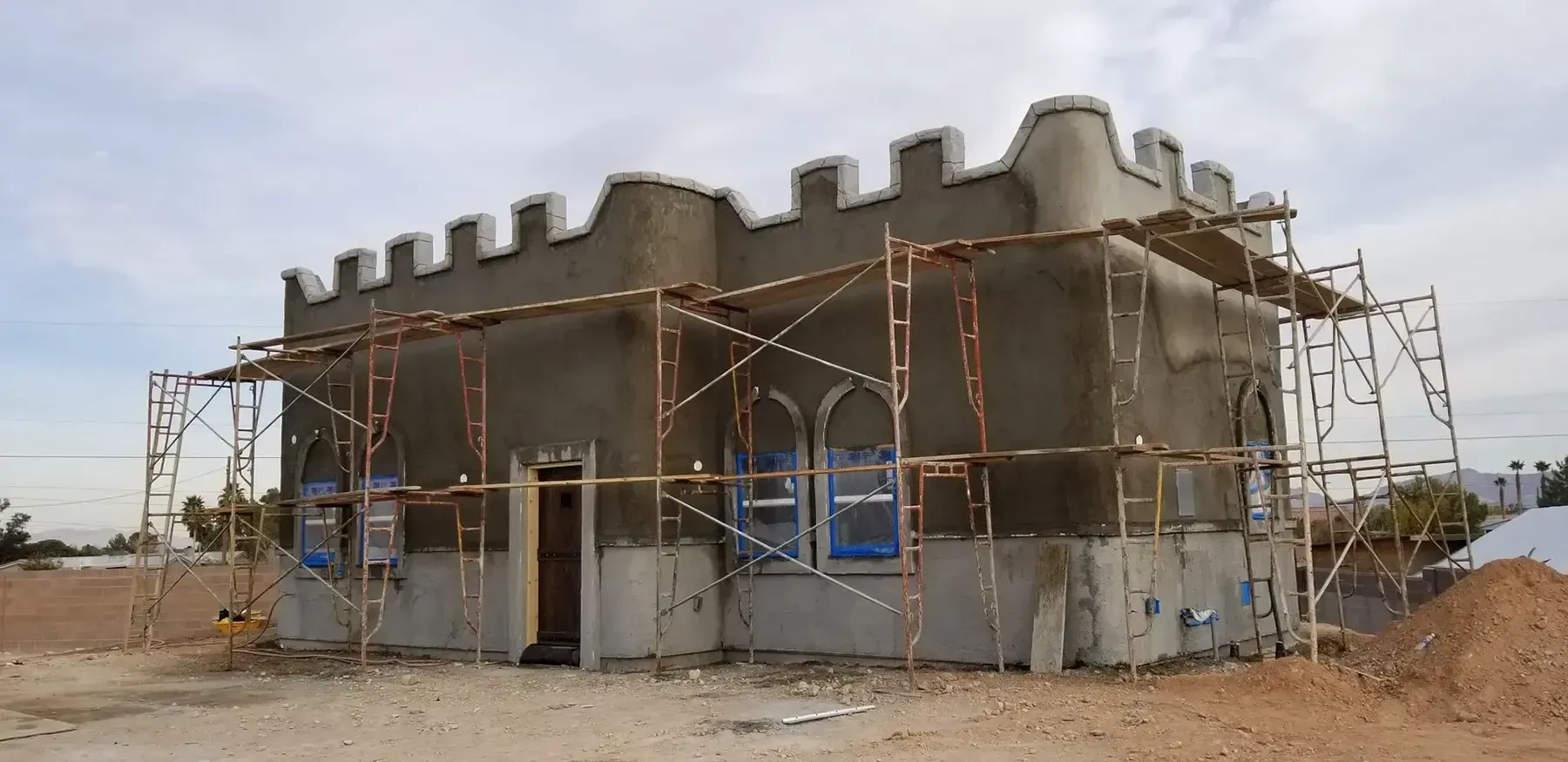 Building under construction with a castle-like design, scaffolding, and arched windows.