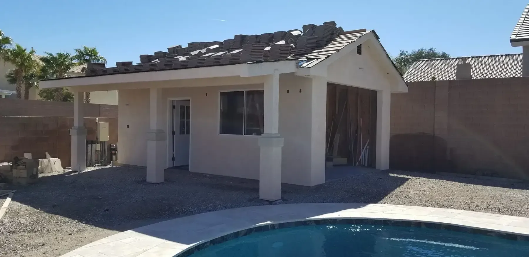 A white building with a brown roof near a swimming pool on a sunny day.