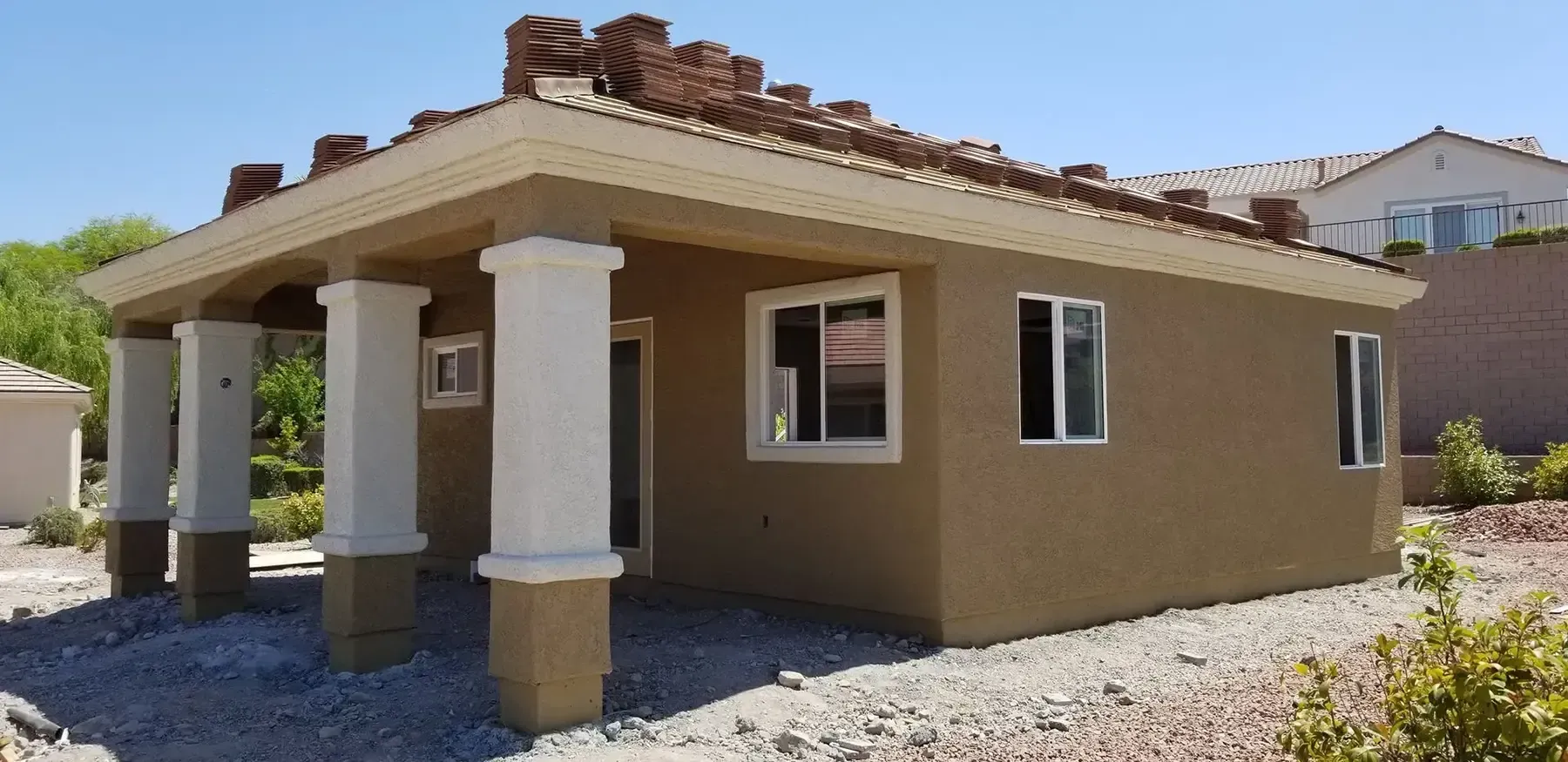 Tan stucco building with columns and windows on a gravel lot under a blue sky.