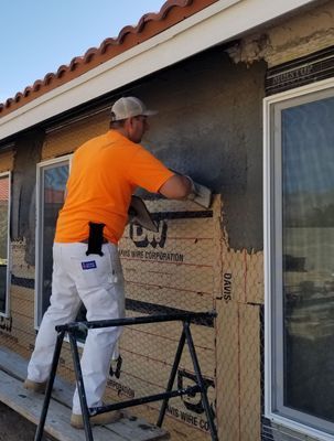 Man in orange shirt applying stucco to a building exterior. 