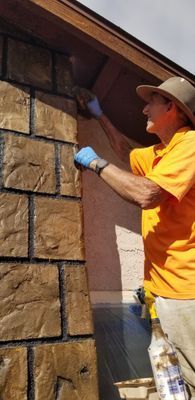 A person painting a wall of faux stone bricks. 