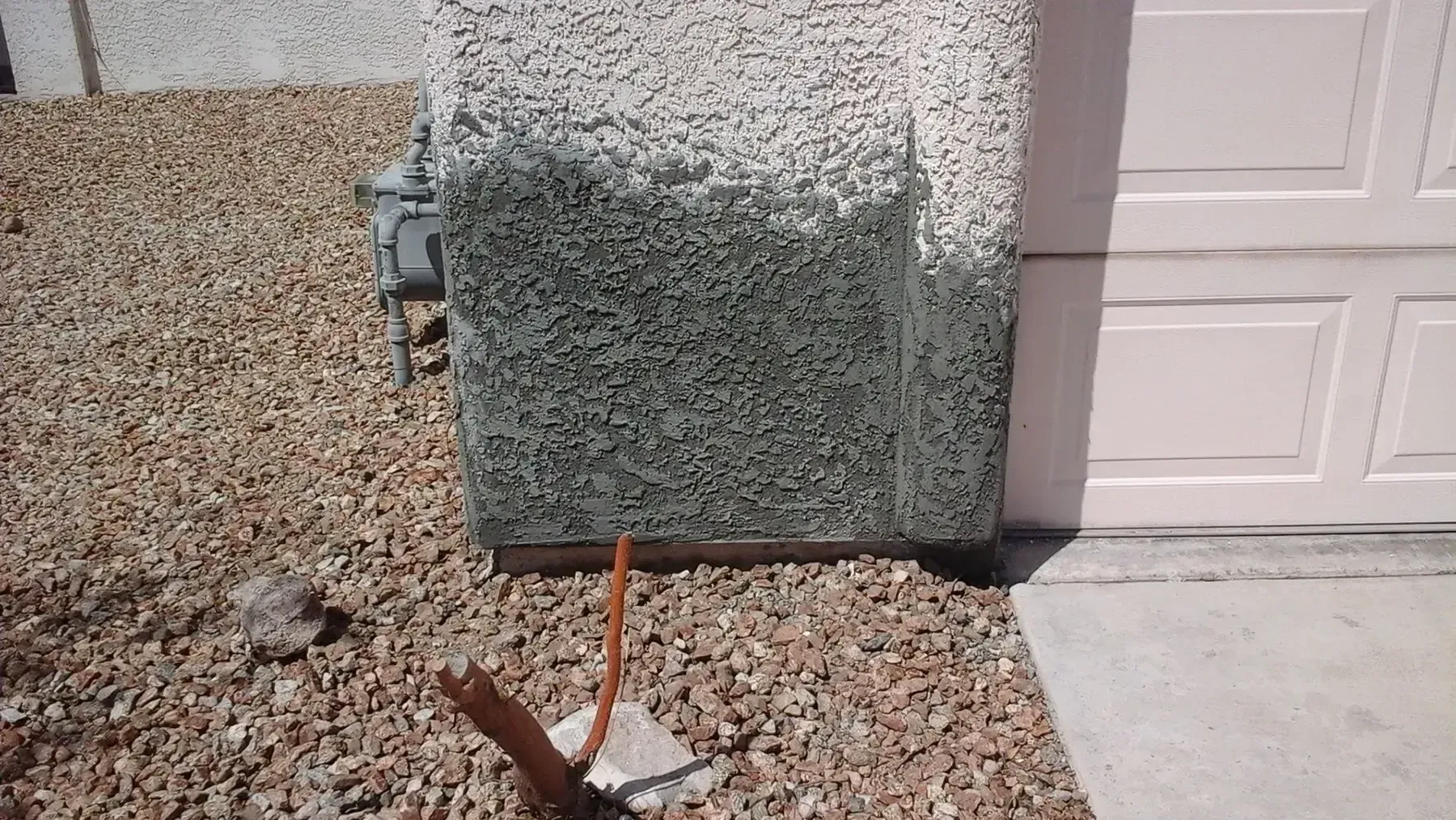 Exterior wall of a house with stucco, partially covered by green growth, next to a garage door.