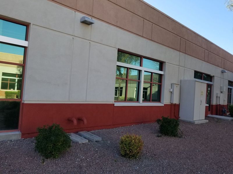 Tan and red building exterior with windows, bushes, and gravel ground.