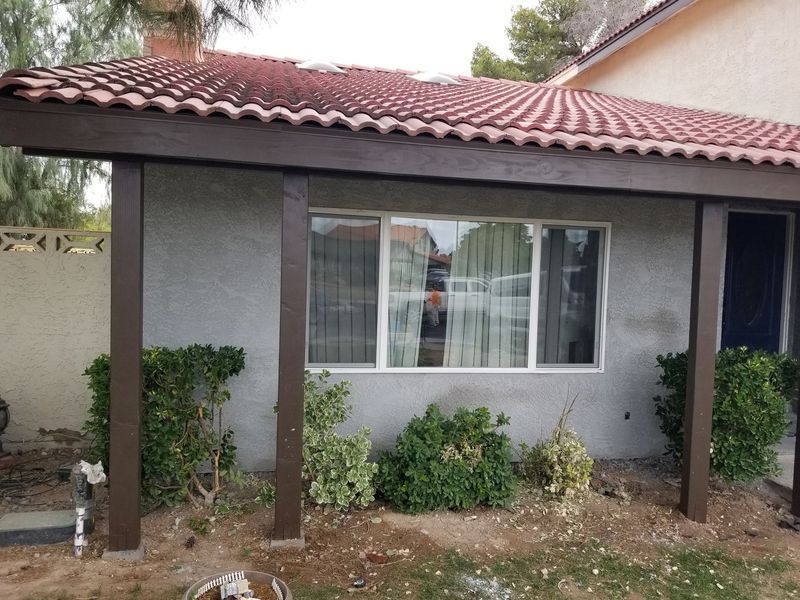 Brown-framed pergola with red tile roof over a window and bushes.