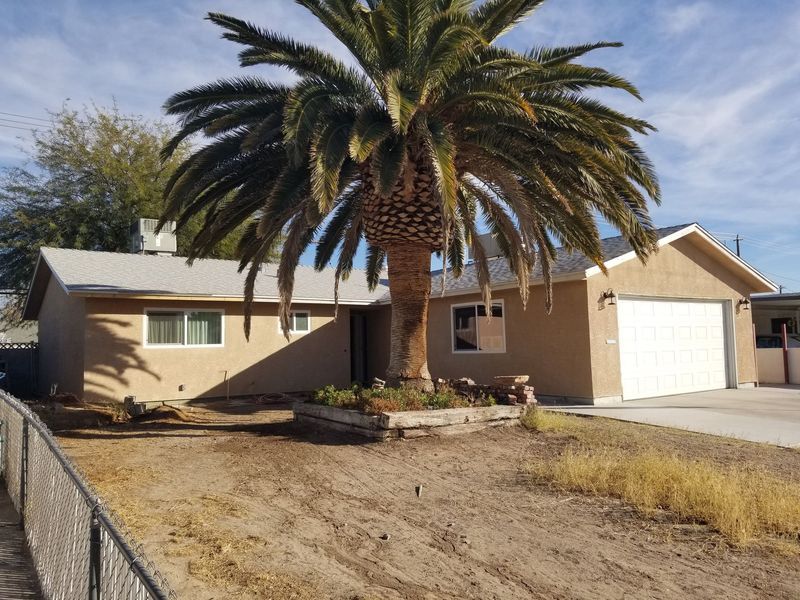 Tan stucco house with palm tree in front yard, gray roof, and two-car garage.