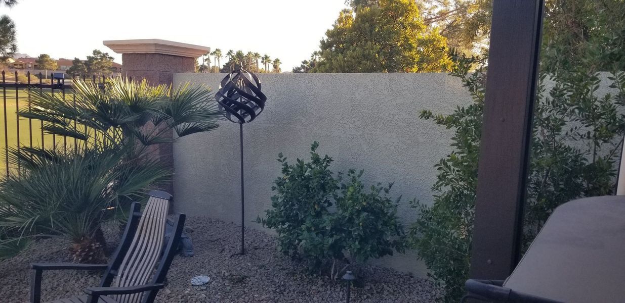 Backyard scene with decorative metal orb on a pole, plants, and a wall.