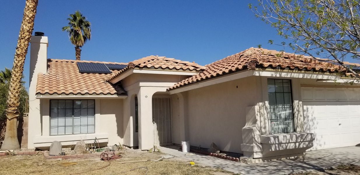 Tan stucco house with terracotta roof tiles, palm tree, and clear blue sky.