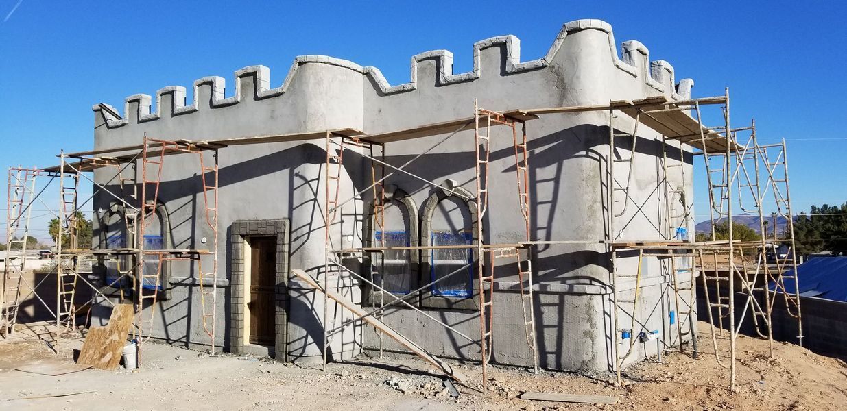 A stone building under construction with castle-like features and scaffolding against a clear, blue sky.